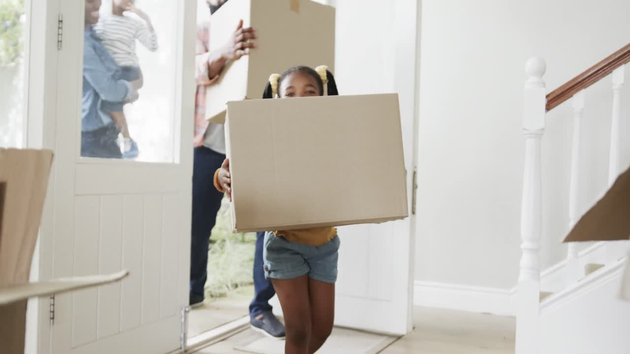 Happy african american couple with son and daughter bringing boxes into house, slow motion