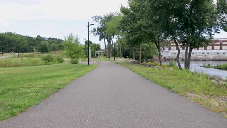 Pov-Zu-Fuß-Auf-Einem-Asphaltierten-Grauen-Weg-Entlang-Eines-Stadtparks-In-Chippewa-Falls,-Wisconsin