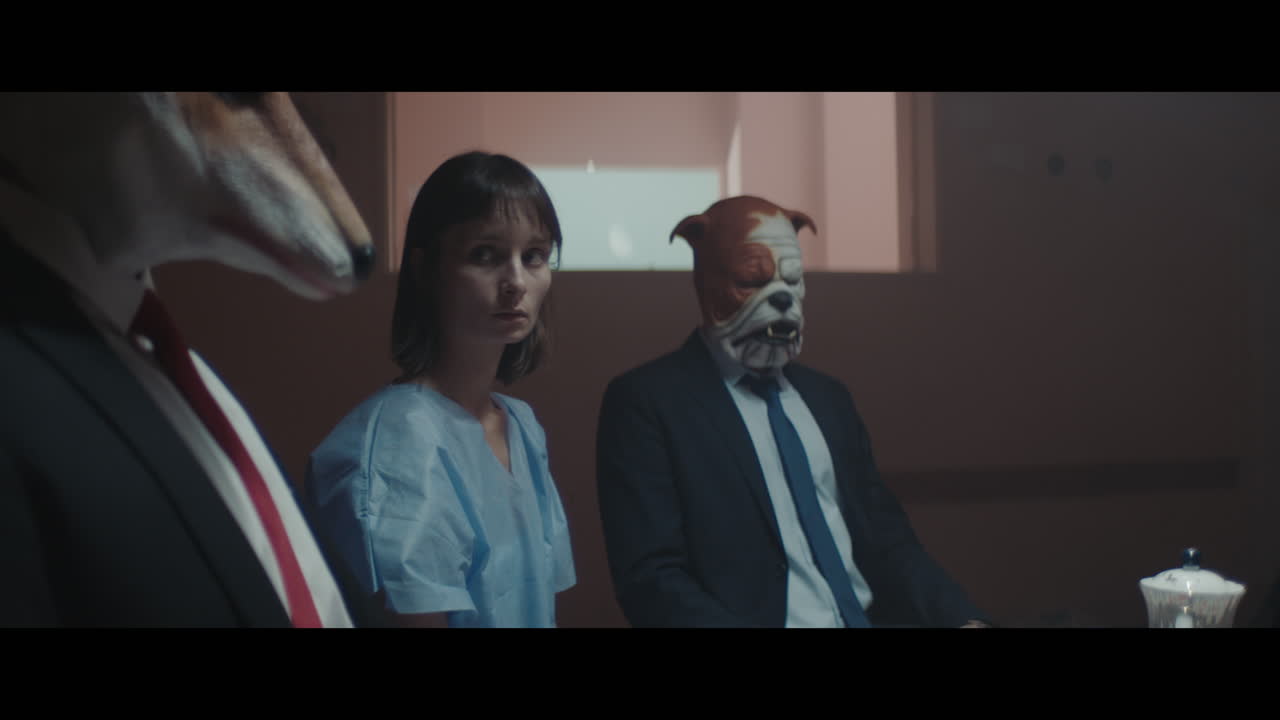 A girl sits at a table with strange figures in animal masks