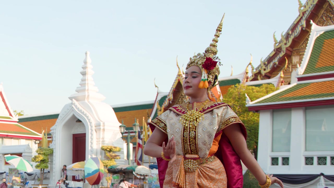 Una ballerina in un elaborato costume dorato esegue movimenti tradizionali Khon fuori da un tempio di Bangkok