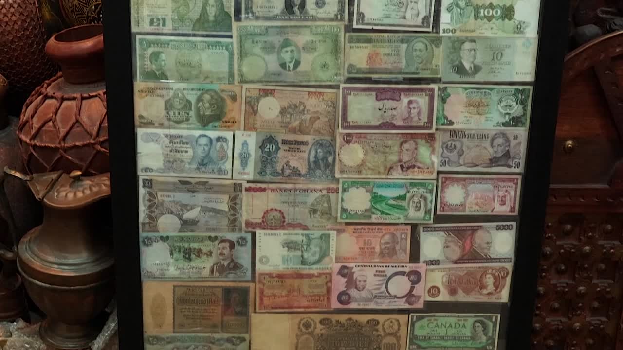 A framed display of diverse global currency banknotes sits among traditional pottery and woodcrafts
