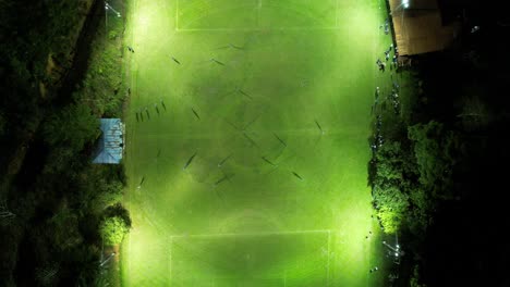 aerial top down of two sport teams playing soccer at night in an illuminated grass field