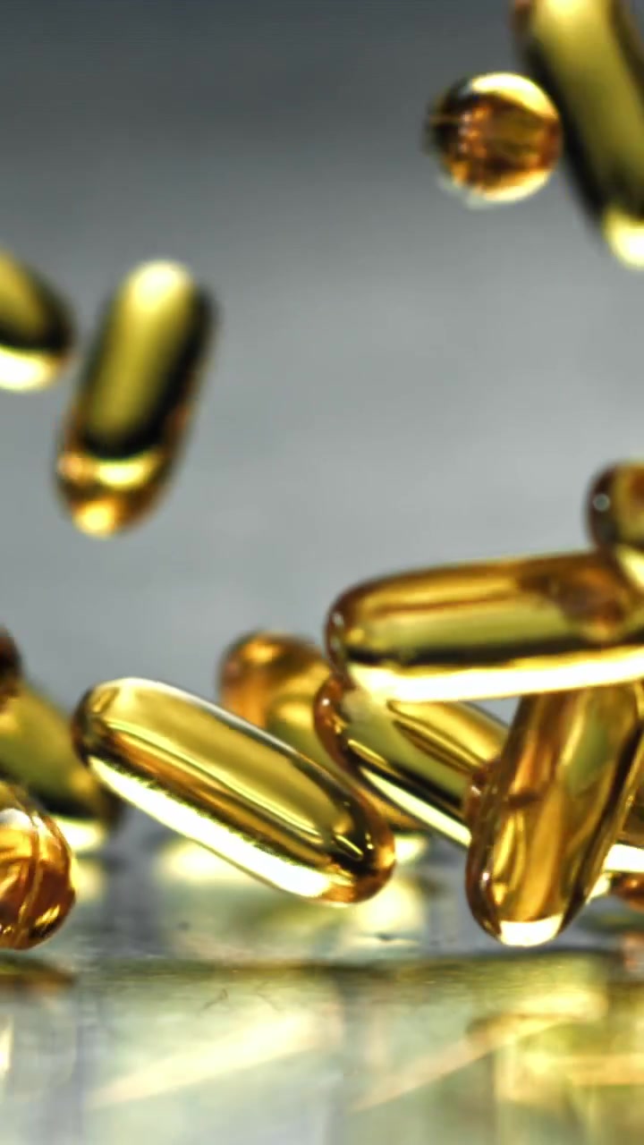 Capsule vitaminiche dorate che cadono al rallentatore su una superficie riflettente