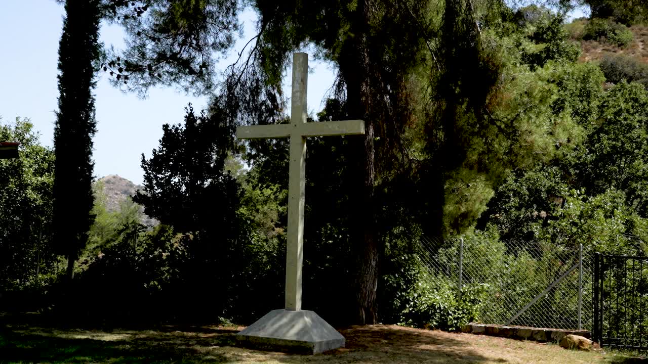A stunning cross rises from the ground surrounded by lush trees and vibrant greenery in a tranquil valley, bathed in warm sunlight, evoking a sense of peace and reflection