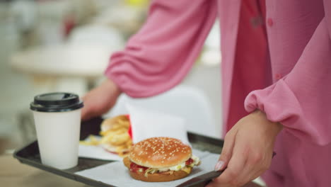 lower body view of woman in pink dress carrying breakfast tray with burger, fries, and drink, walking toward her table, drops the the tray before sitting down, with blur background