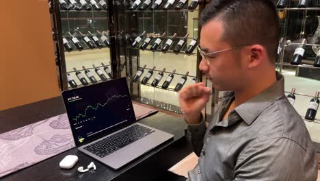 rich asian millennial man pumping fists, celebrating stock market gain inside luxurious home