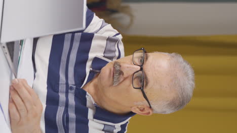 Vertical-video-of-Home-office-worker-old-man-working-seriously-and-focused.