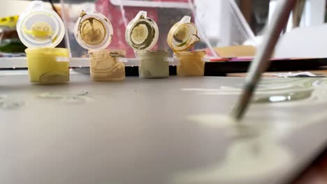 disparo de cerca de tubos de pintura abiertos con un pincel de pintura ocupado pintando en un lienzo blanco