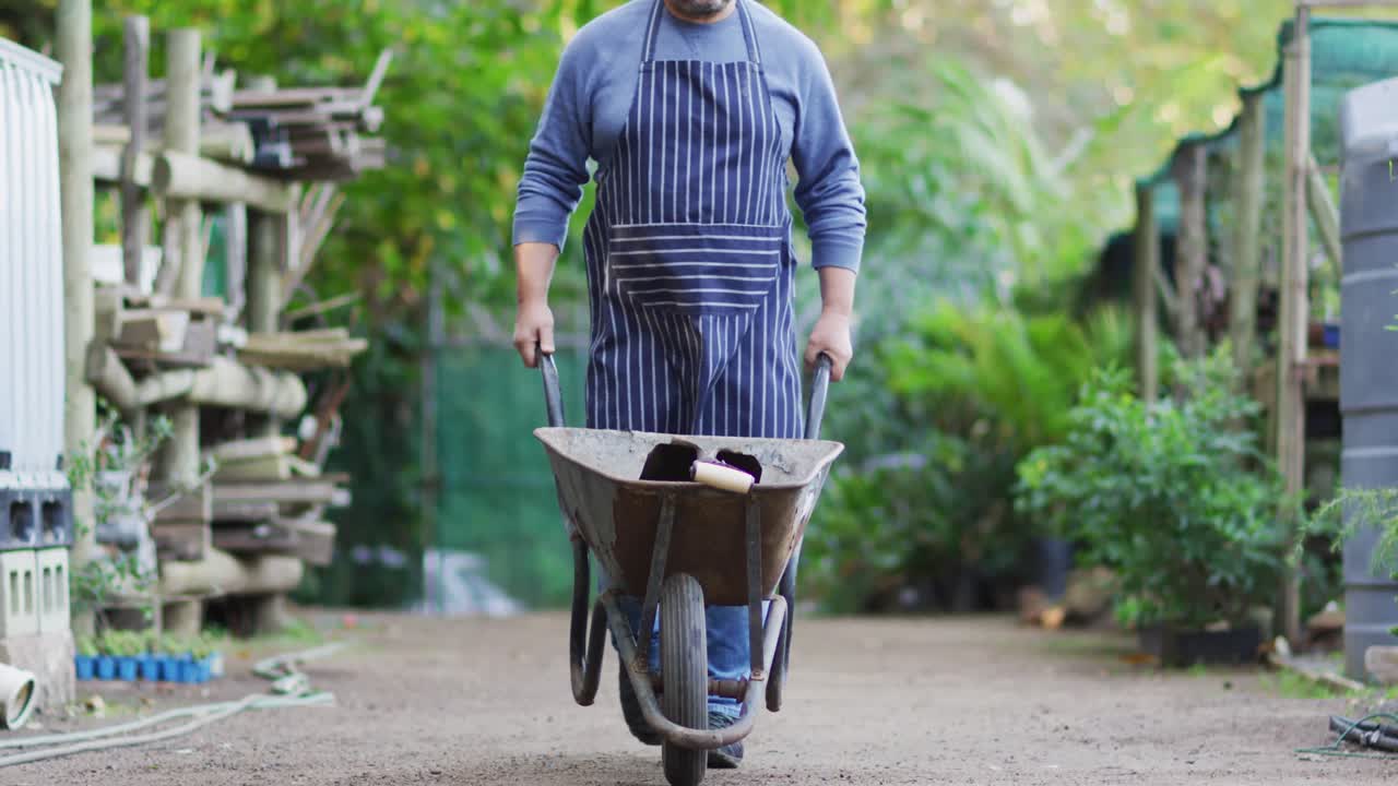 jardinero caucásico caminando con una carretilla en el centro del jardín