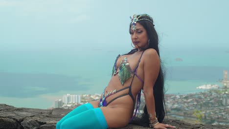 primer plano de una mujer en un disfraz de carnaval sentada en un fuerte con una costa caribeña en el fondo