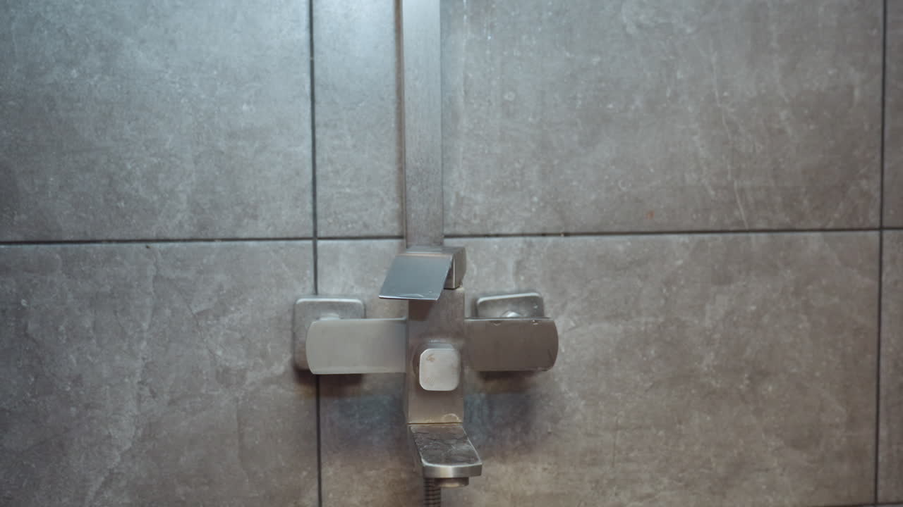 close up of hand returning handheld shower to wall mount as residual water drips from fixture onto ceramic tiles capturing gentle drip motion and serene bath environment in modern tiled shower