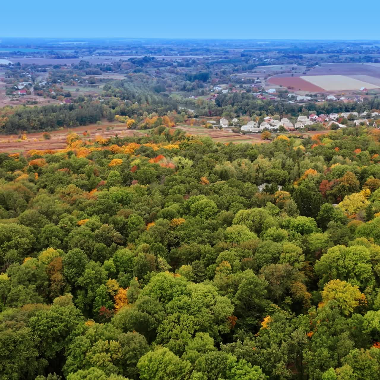 Green woods neighboring near the picturesque village and agricultural fields. Hazy horizon at backdrop
