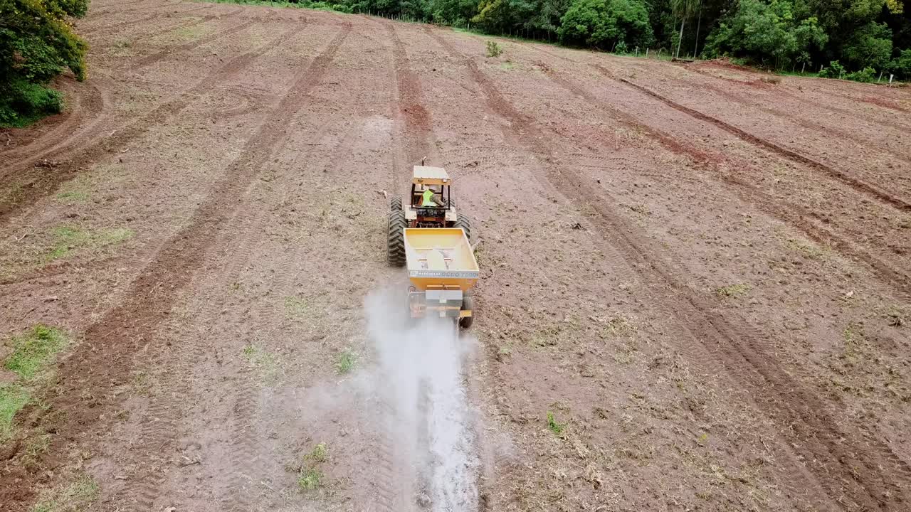 Luftoptagelse, der følger en traktor, mens den spreder kalk eller gødning på en nyligt pløjet mark, der forbereder jorden til plantning
