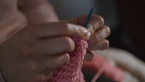 extreme close up of woman's hands knitting a pink piece of clothing