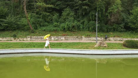 Aerial-sideways-shot,-walking-woman-in-white-dress-and-yellow-umbrella