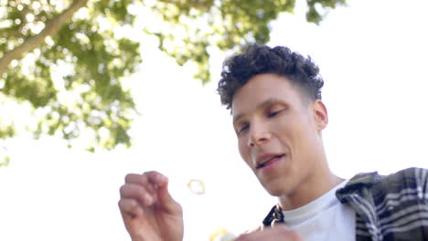 Happy-biracial-man-blowing-bubbles-in-sunny-garden,-in-slow-motion