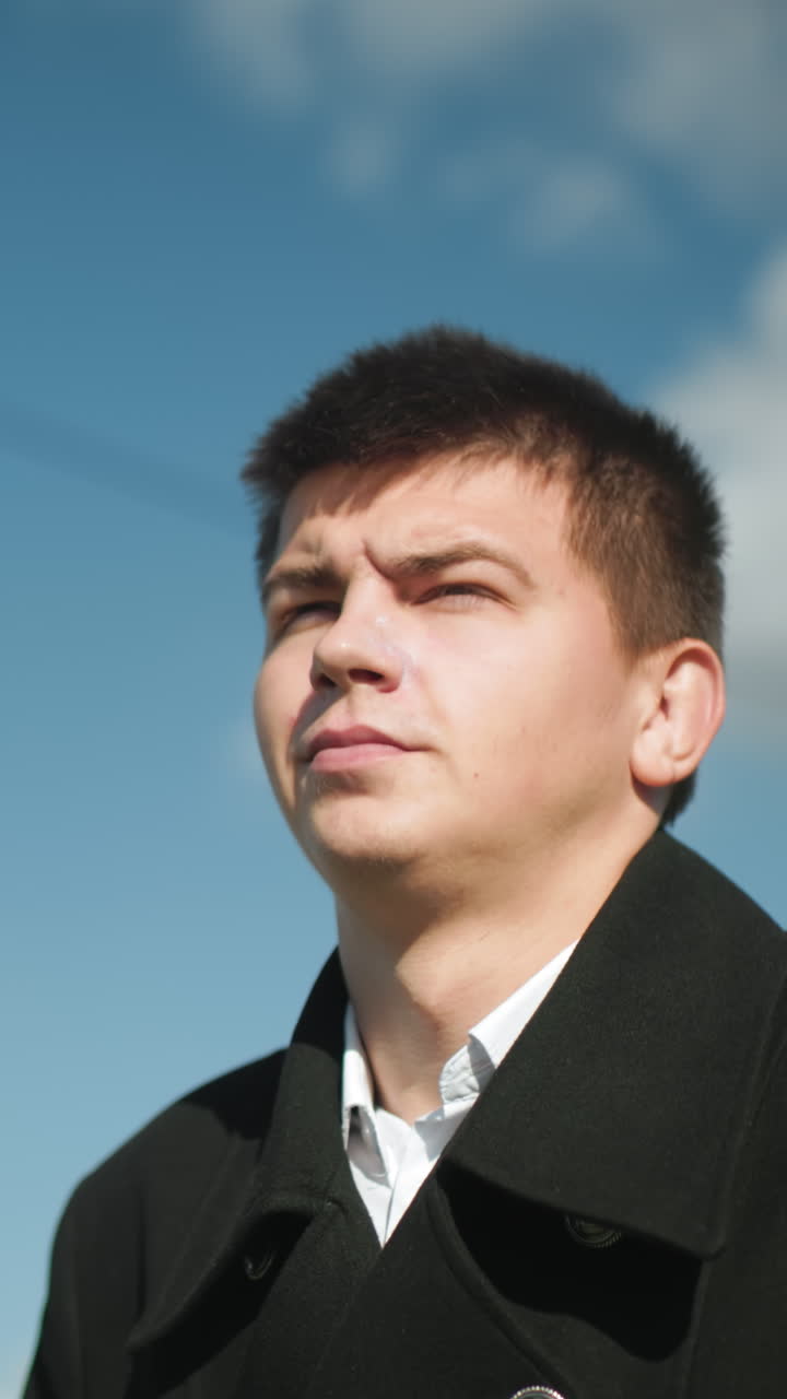 검은 코트를 입은 변호사가 밝은 하늘 아래 밖에서 자신감 있게 고 있으며, 빛이 반사되어 도시 환경에서 흐릿한 전선과 뒷면에 소나무가 있습니다.