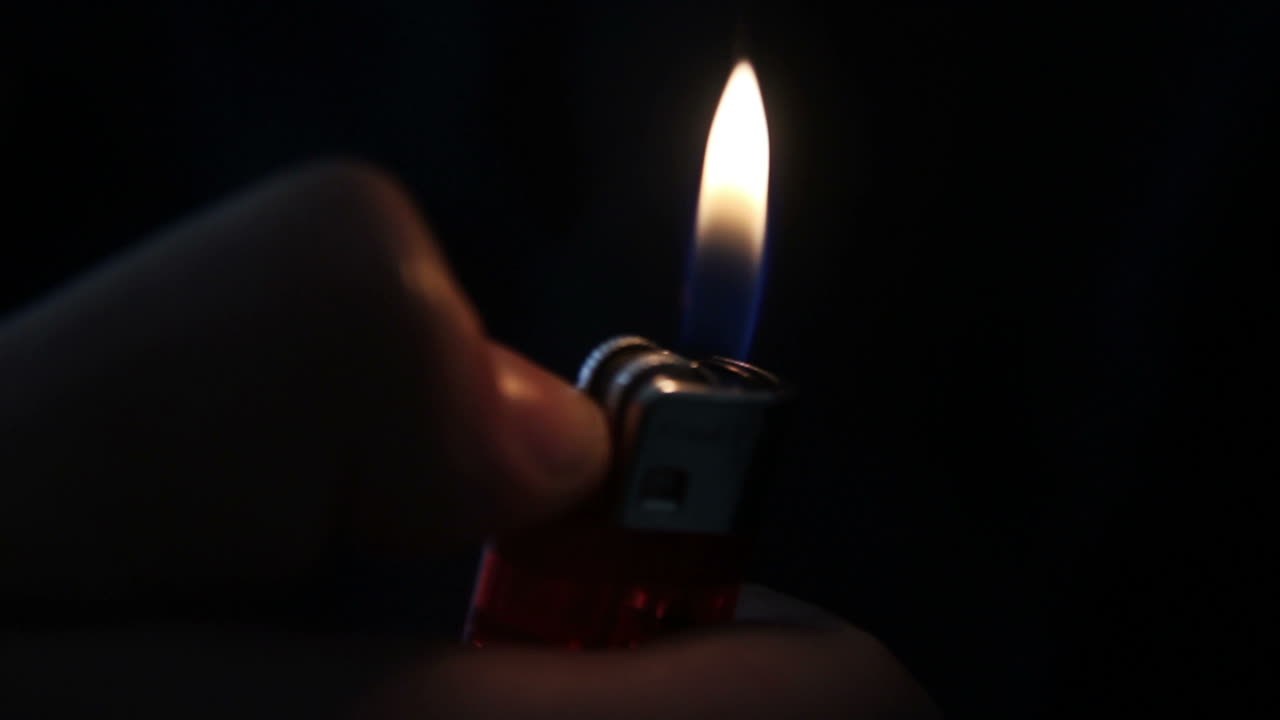 Close-Up of Hand Lighting a Red Lighter in the Dark