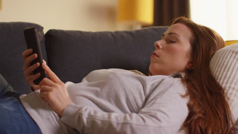 close up of woman lying on sofa at home at streaming or watching movie or show or scrolling internet on mobile phone 6