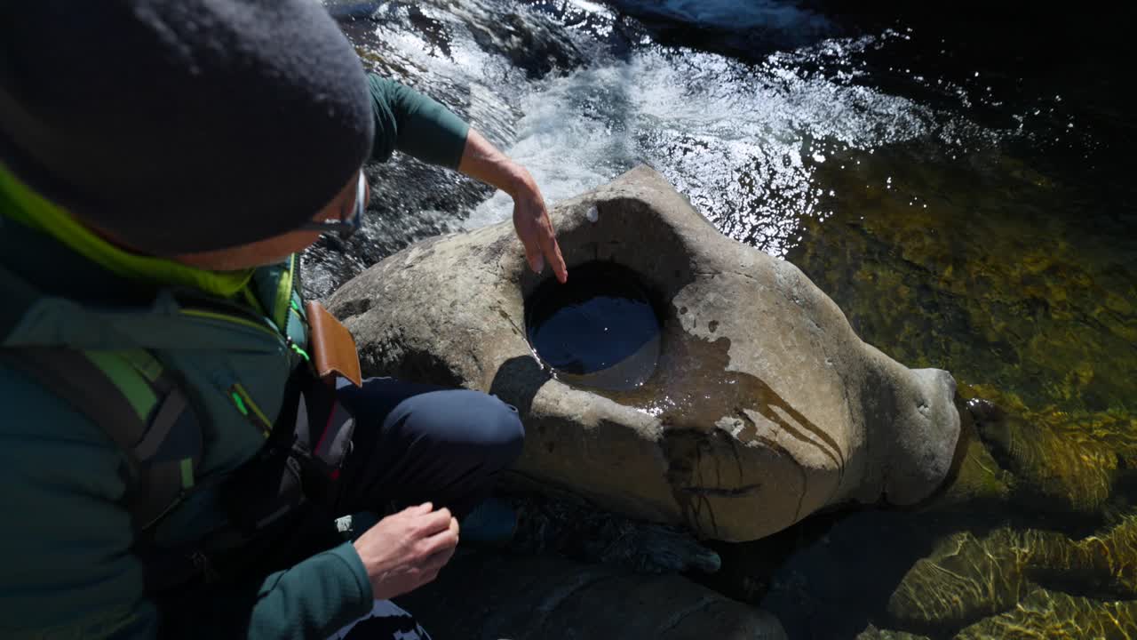 Hiker Measuring Depth Of Water In Round Hole Carved Into Riverside Rock In Noli, Italy. high angle shot