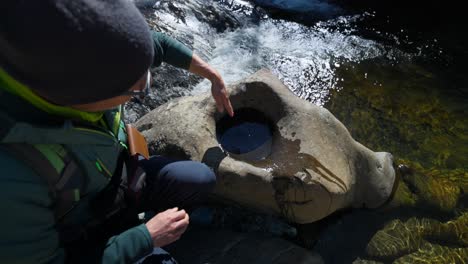 hiker measuring depth of water in round hole carved into riverside rock in noli, italy. high angle shot