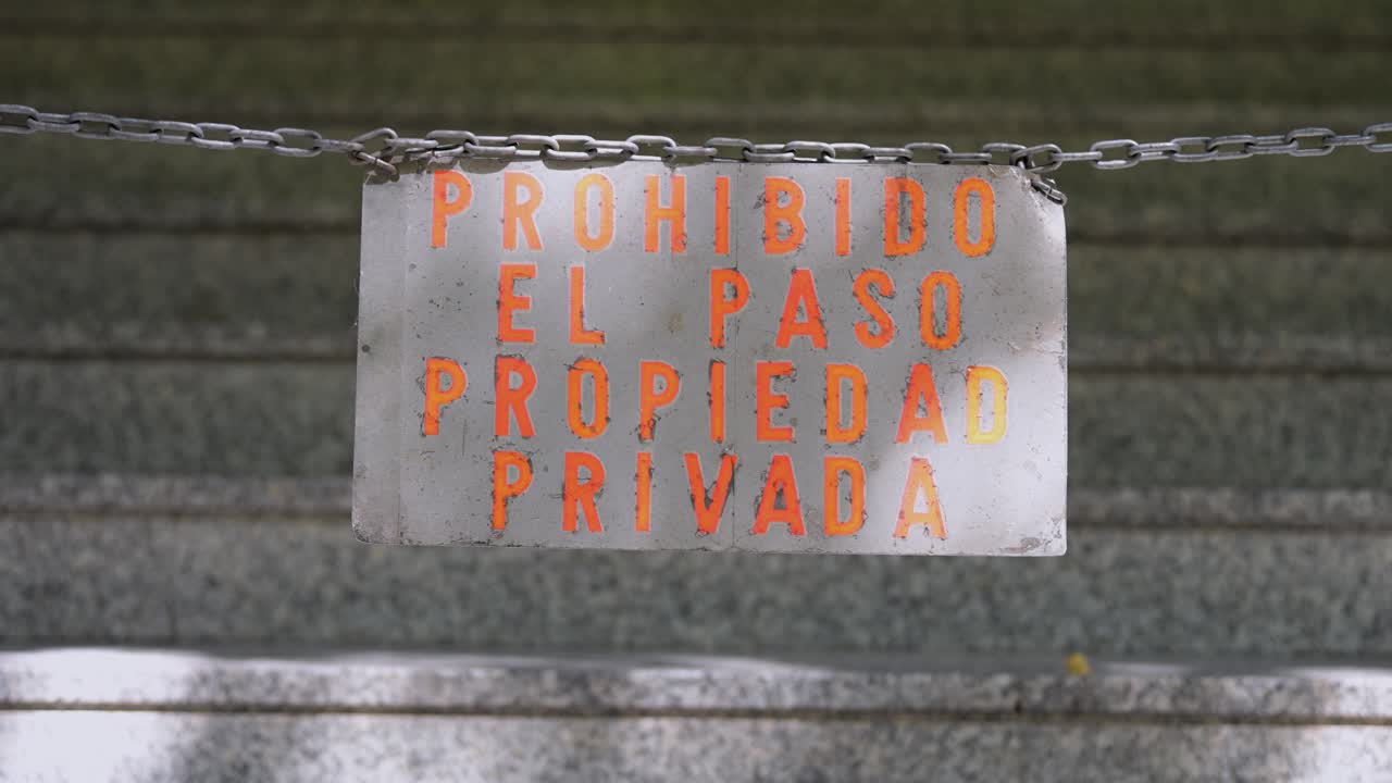 A weathered sign in Spanish reads "Prohibido El Paso, Propiedad Privada" (No Trespassing, Private Property). A chain physically blocks access, reinforcing the warning