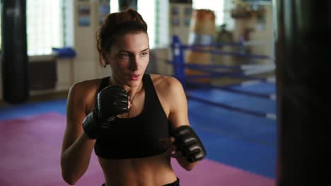 caucasian female boxer hitting the boxing bag with her hands in gloves in the gym alone. tough power training of a female