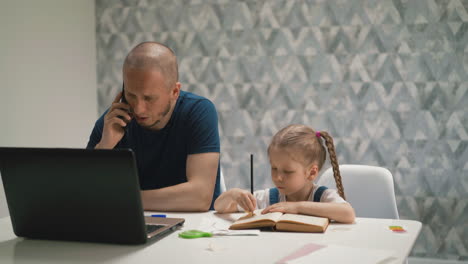father talks on phone trying to work daughter does homework