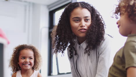 Young-female-teacher-talking-with-infant-school-kids-in-the-classroom,-low-angle,-close-up