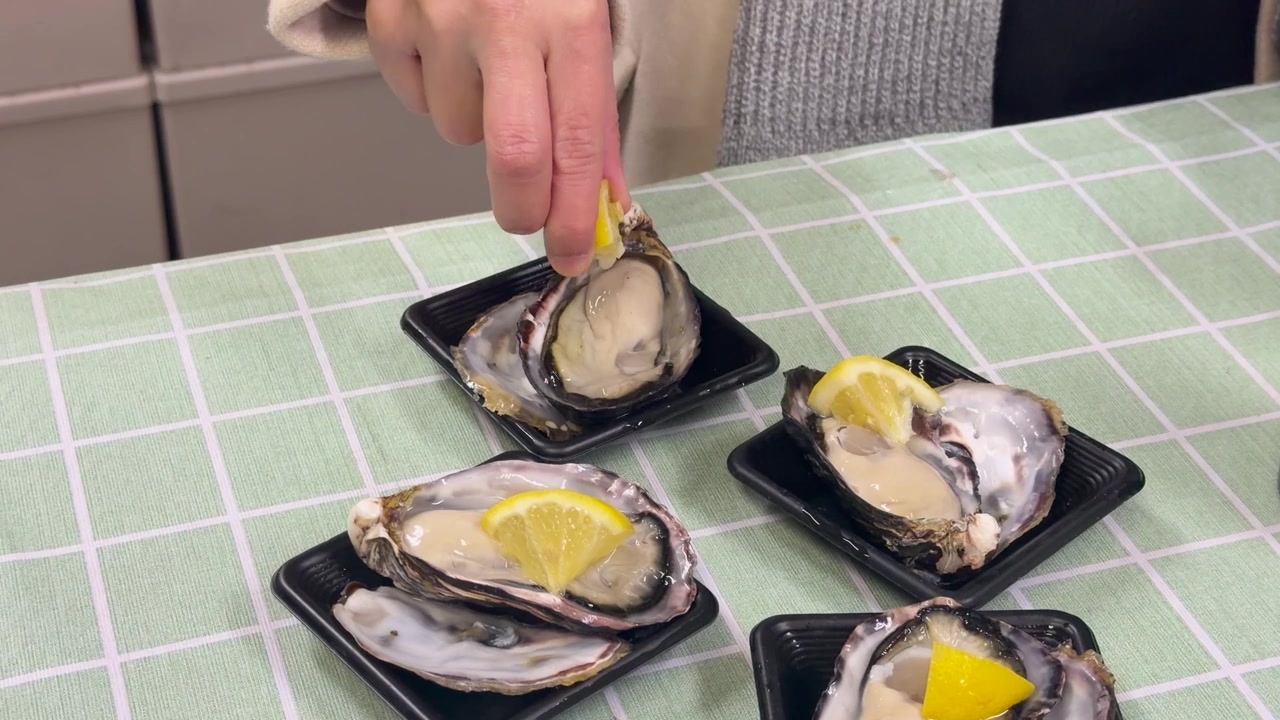 A close-up shot shows a hand squeezing lemon juice onto fresh raw oysters in Japan