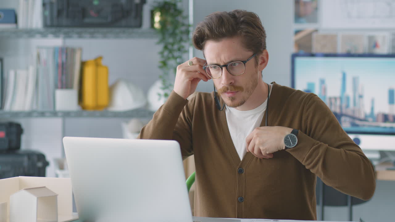 arquitecto masculino en la oficina escuchando música en auriculares inalámbricos mientras usa una computadora portátil