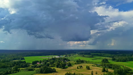 beautiful landscape of a green field surrounded by trees under the blue and grey clouds of summer rain