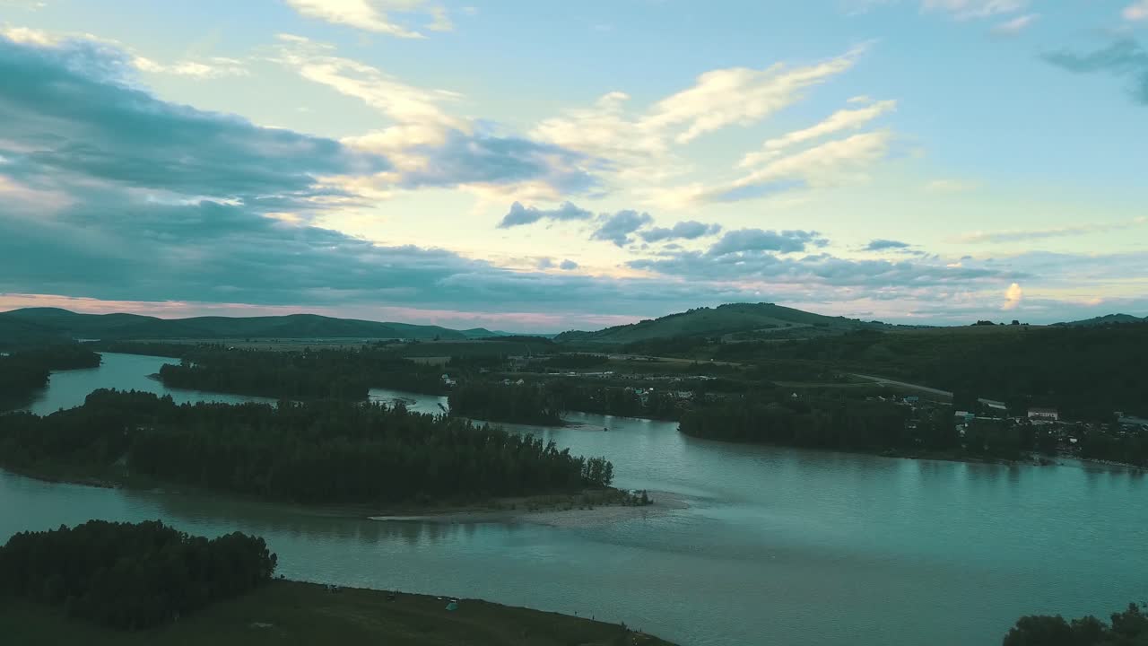 Pemandangan udara kota wisata kecil di pegunungan di bawah awan saat matahari terbenam di dekat sungai pegunungan.