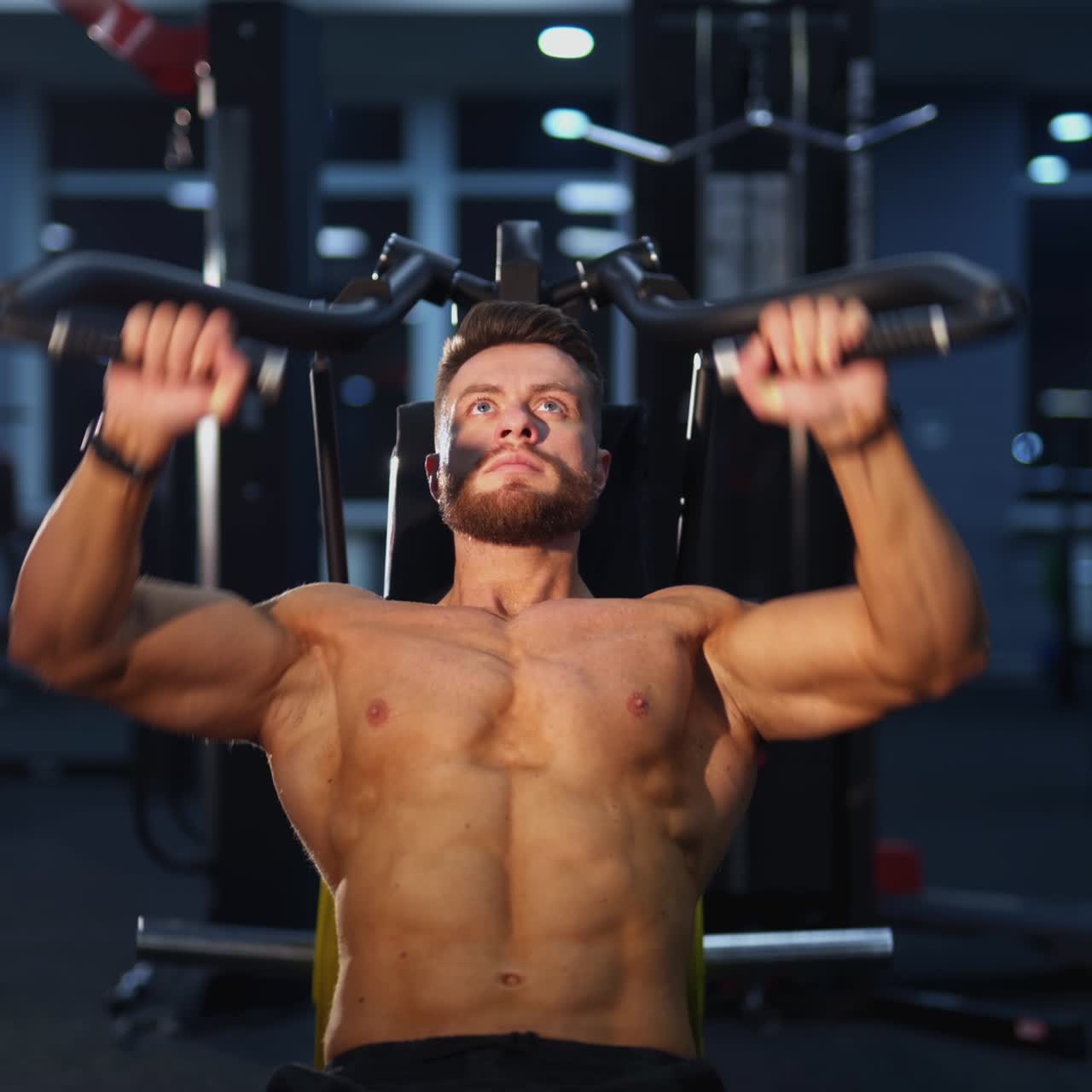 Training muscles. Sportsman pumping his trained body on a simulator. Strong trainer doing workout. Bodybuilder doing exercise on the modern simulator in the gym