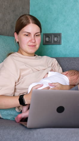 caucasian young woman combining work and childcare. mother of infant feeds a baby and works on laptop.. vertical video