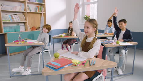 multiethnic group of kids in classroom raising hands during english class 1