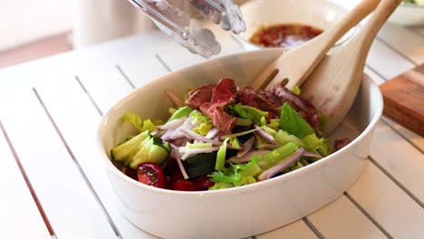 a sequence showing beef being added to a vibrant salad. bright lighting highlights fresh vegetables and a modern kitchen setting