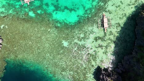 Aerial view of traditional Filipino boats floating above the vibrant turquoise waters and coral reefs of Twin Lagoon, Coron, Philippines, revealing the area's clear water and tropical beauty