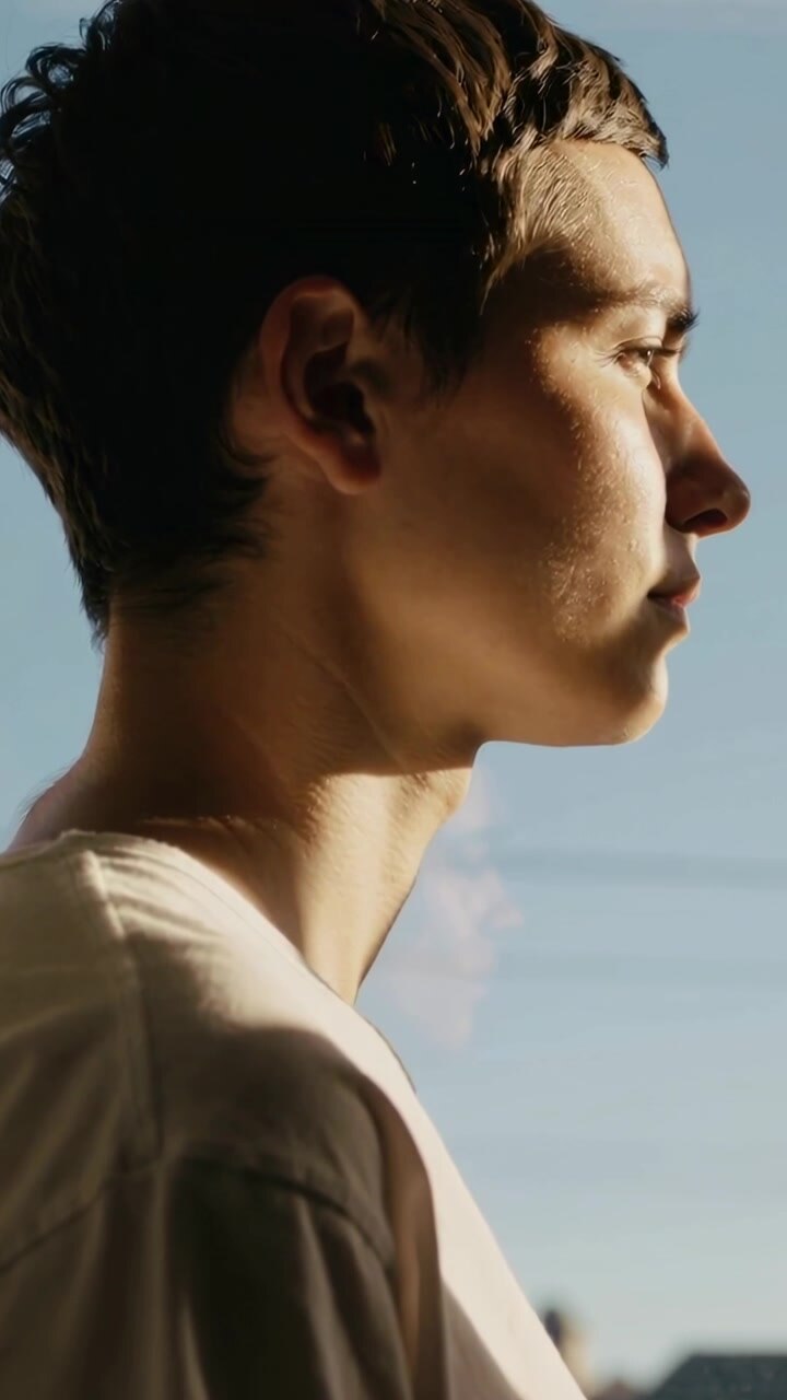 Vertical video: Gazing Asian teen tilting head at window as low sun catching face, in white T-shirt