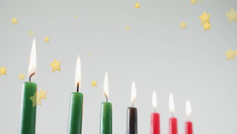 animation of golden stars falling over kwanzaa candles on grey background