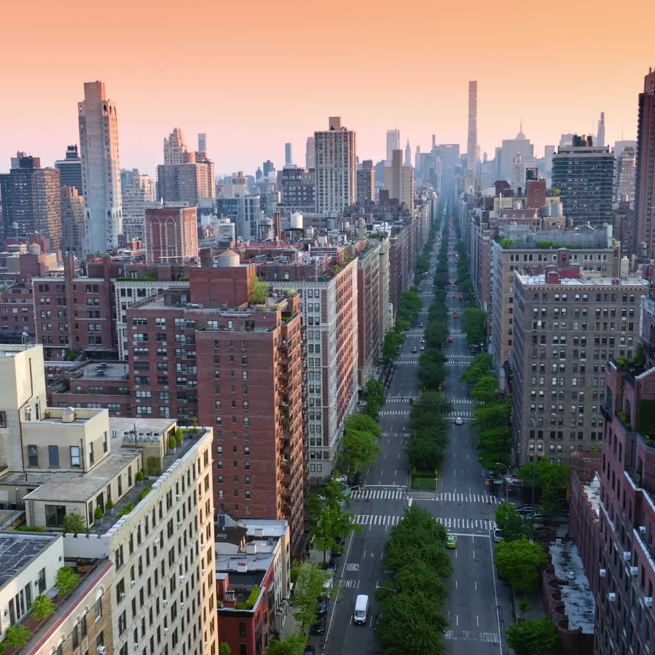 Very long street with greenery on both sides and middle. High buildings and skyscrapers against pink sky