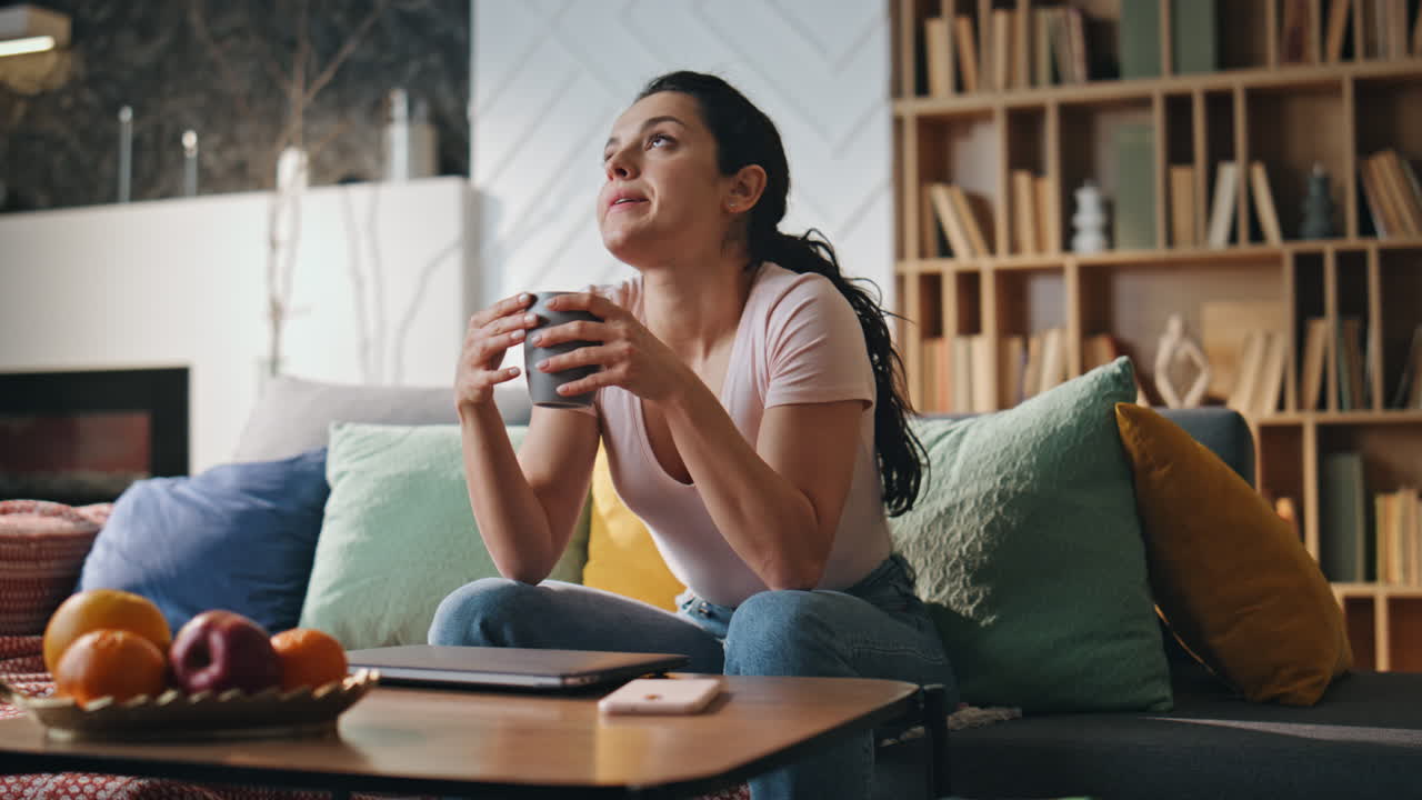 Tired woman drinking coffee after remote laptop work late evening. Girl relaxing