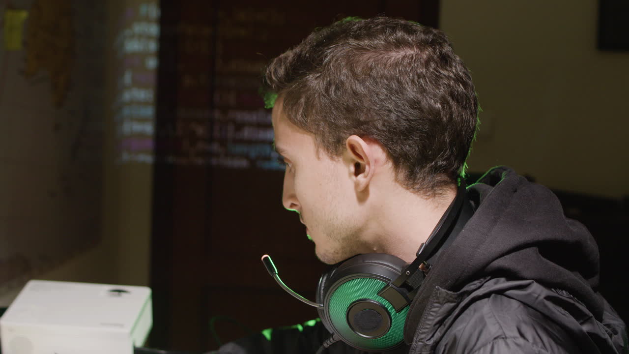 Side view of a Caucasian hacker at late night working on computer and stealing network database data