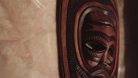 a native wooden tribal face mask hanging on the wall - close up shot