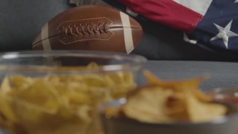 person at home watching american football game on tv with snacks and ball