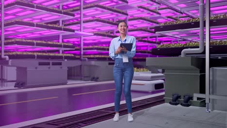 vista lateral completa del cuerpo de una trabajadora profesional asiática de pie con su tableta en una granja vertical, instalación industrial de alta tecnología, escribiendo y decepcionada con asintiendo con la cabeza