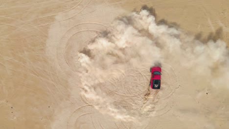 Camión-Rojo-Haciendo-Donuts-En-La-Arena-Del-Desierto,-Vista-Superior-Aérea