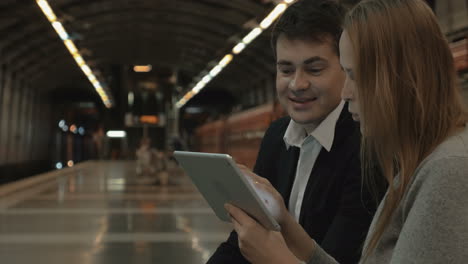 una pareja con una tableta esperando el tren del metro.