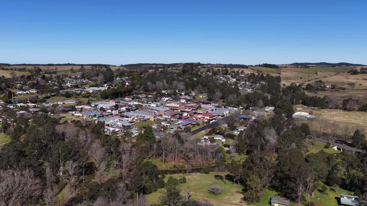 Drone ascends over Dorrigo, revealing rural town, farmland, clear sky, and community buildings