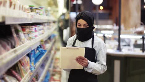 Mujer-Con-Bufanda-Negra-Trabajando-En-La-Tienda,-Inspeccionando-Estantes-Con-Tableta